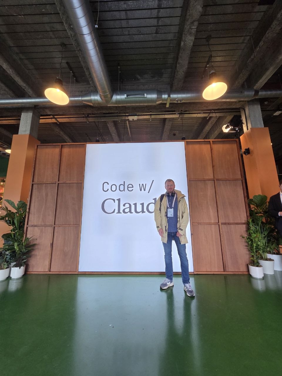 The author standing in front of a large Code w/ Claude wall at the venue.