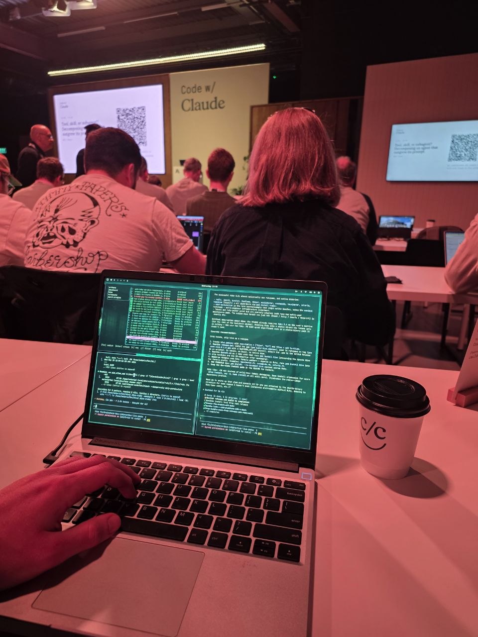 A laptop in the audience with a terminal multiplexer running an agentic workflow during a talk.
