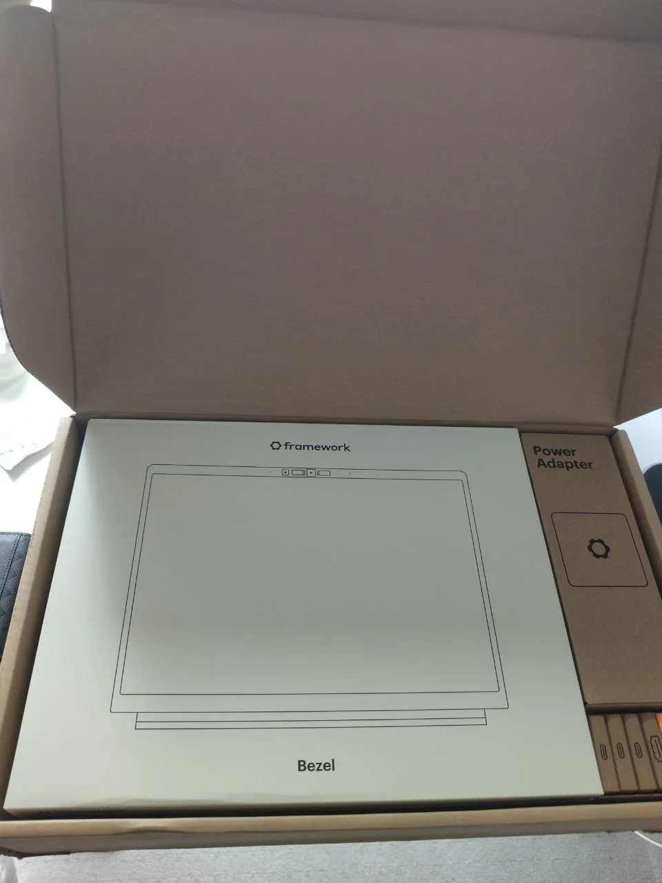 An open Framework shipping box with the bezel, power adapter, and expansion cards packaged separately.
